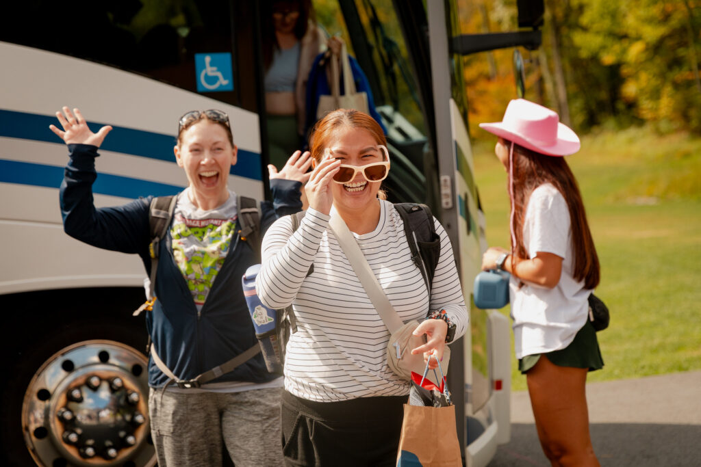 Two women in long sleeves short smiling as they get off the bus