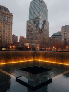 9/11 Memorial reflecting pool with city skyline at dusk in New York City.