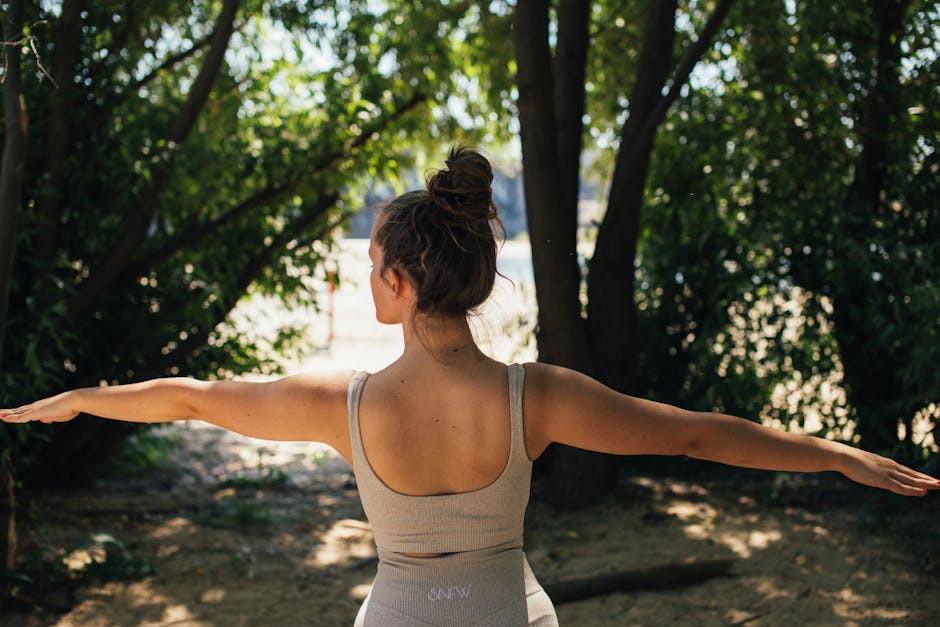 Back view of a young woman in activewear practicing yoga outdoors surrounded by trees.