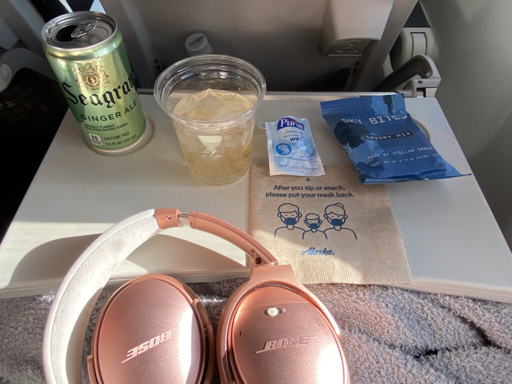 A can of Seagrams ginger ale, airplane snacks, alaska airlines napkin, pink Boss headphones